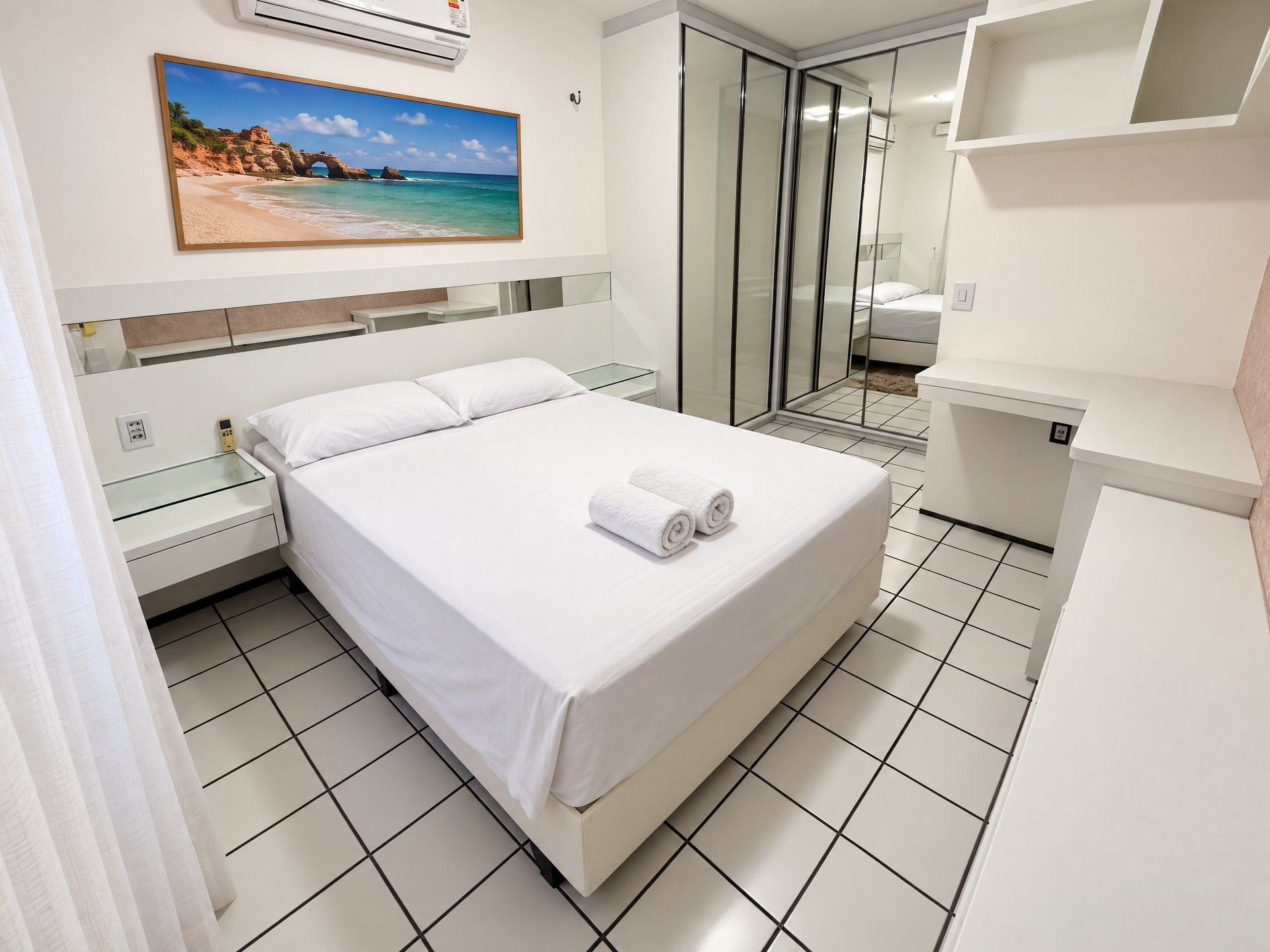 A hotel room with a bed, a bedside table, a glass shower enclosure, and a painting of a beach scene.