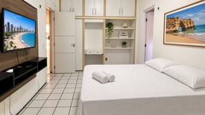 A hotel room with a bed, a TV, a wardrobe, and a painting of a beach. - Ape Familia 3 Quartos 200m da Feirinha Beira mar (Fortaleza)