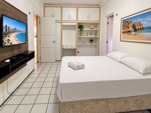 A hotel room with a bed, a TV, a wardrobe, and a painting of a beach. - Ape Familia 3 Quartos 200m da Feirinha Beira mar (Fortaleza)