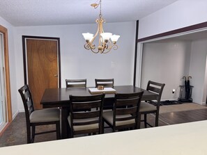 A dining room with a wooden table, four chairs, a chandelier, and a door. - Spacious Family-Friendly 3BR home in Juneau, minutes from the Airport! (Juneau)
