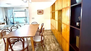 Un coin repas avec une table et des chaises en bois, un sol en marbre et une bibliothèque agrémentée d’objets décoratifs.