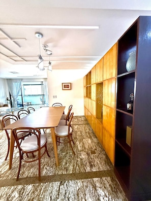 A dining area with a wooden table and chairs, a marble floor, and a bookshelf with decorative items. - Apto Preferido Pelas Familias, 200m da Beira mar (Fortaleza)