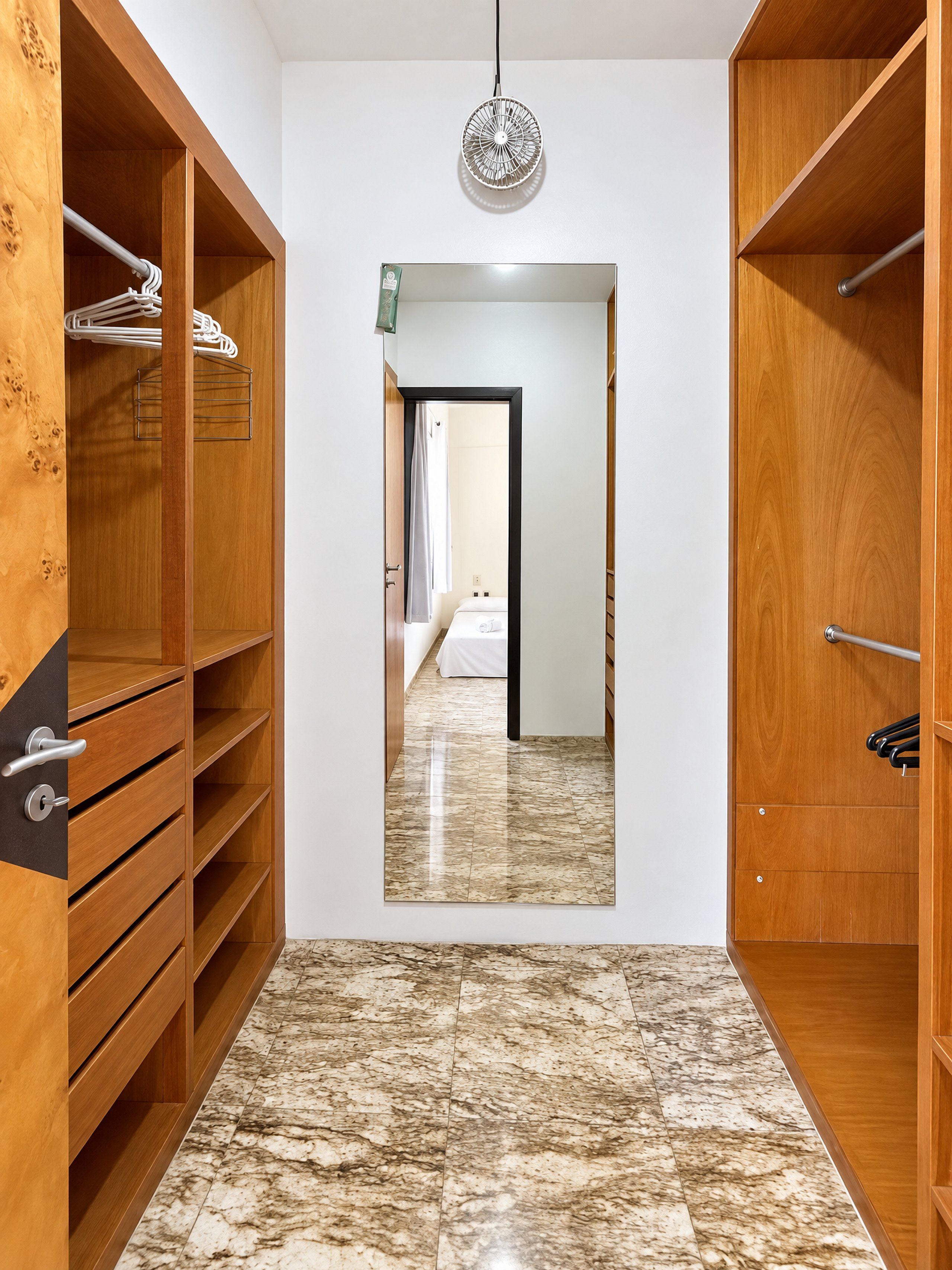 A hallway with wooden shelving units, a marble floor, and a door leading to another room.