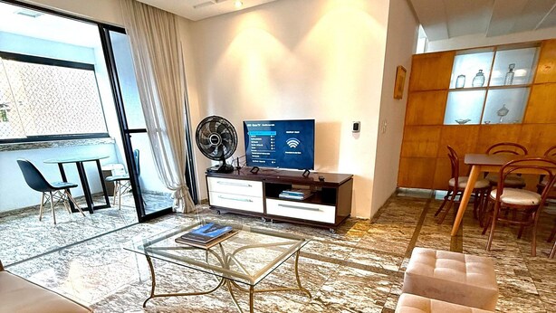 Une chambre d’hôtel moderne équipée d’un canapé, d’un pouf, d’une télévision, d’un ventilateur et d’un coin repas avec des chaises et une table.