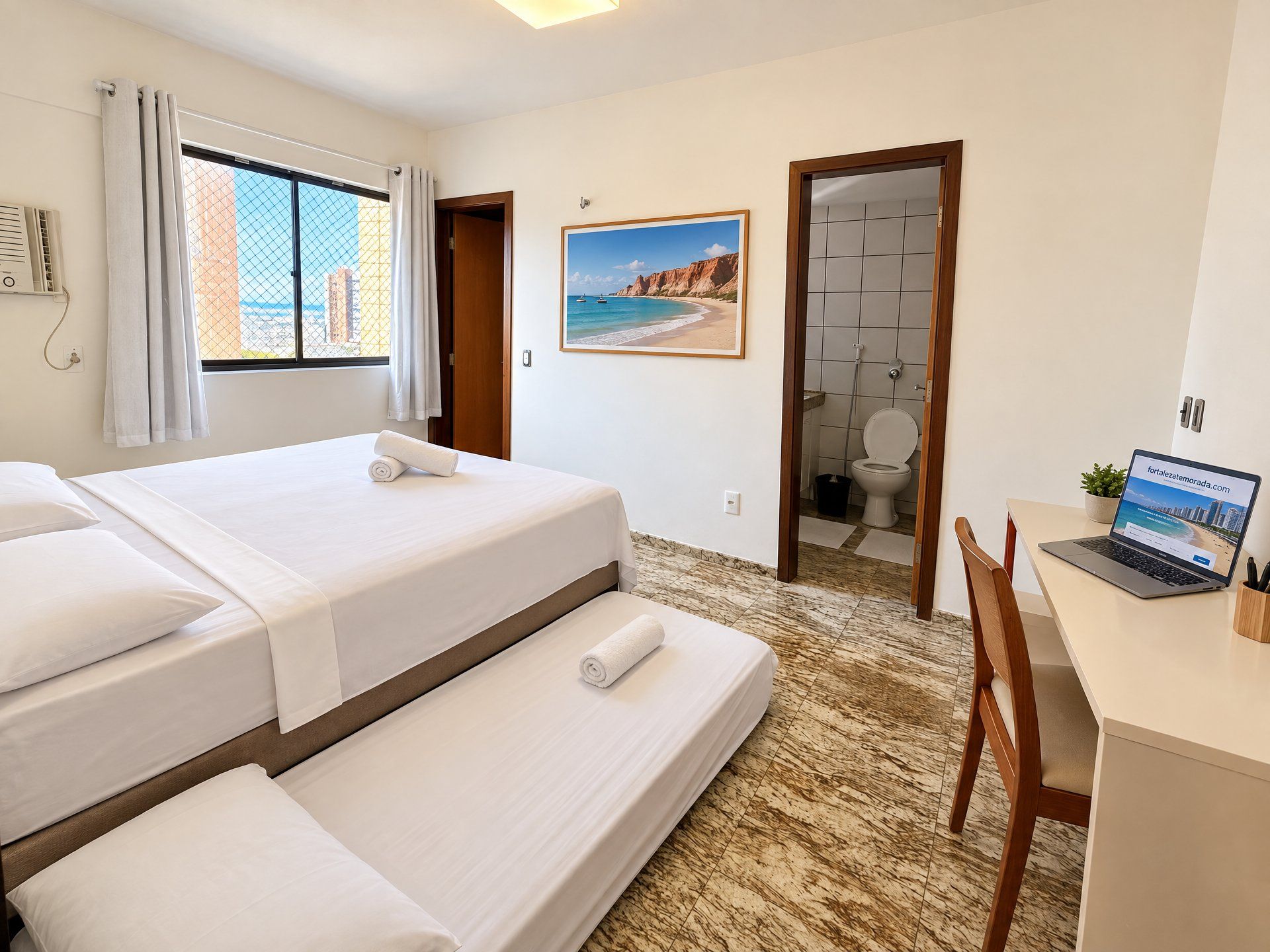 A hotel room with a bed, a desk with a laptop, a shower, and a window with curtains.