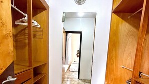 Un couloir doté d’étagères en bois, d’un sol en marbre et d’un miroir qui reflète une pièce avec un lit et une porte.
