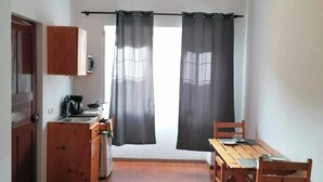 A compact living space with a kitchenette, a dining area, and a view through a window with curtains.