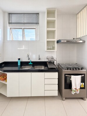 A modern kitchen with a gas stove, double sink, and white cabinetry. - Apartamento Familia Todo Reformado 4 Quartos (Fortaleza)