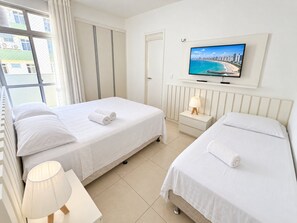 A hotel room with two beds, a TV on the wall, and a window with curtains. - Apartamento Familia Todo Reformado 4 Quartos (Fortaleza)