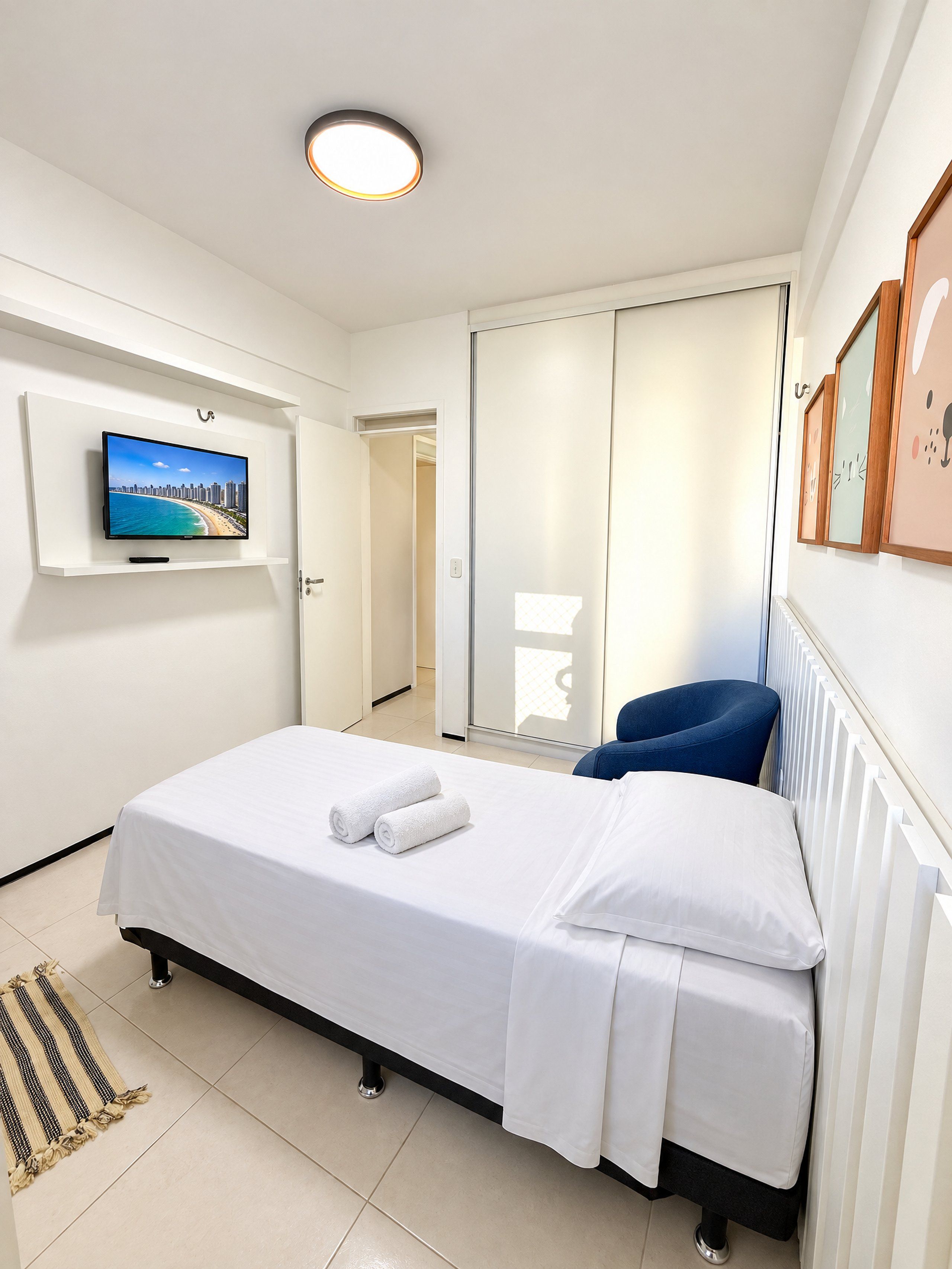Una habitación de hotel con una cama, un televisor montado en la pared, un armario con puerta corredera y un cuadro enmarcado.