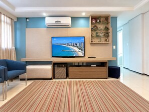 A living room with a flat-screen TV, a sofa, a coffee table, a TV stand, and a patterned rug. - Apartamento Familia Todo Reformado 4 Quartos (Fortaleza)