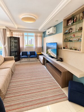 A modern living room with a sofa, a TV, a coffee table, and a bookshelf. - Apartamento Familia Todo Reformado 4 Quartos (Fortaleza)
