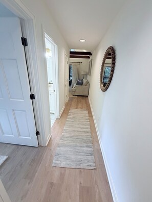 A hallway with a wooden floor, a white door, a white wall, and a beige sofa in the background. - Merry Mariner of Kiawah-100 ft to beach boardwalk-Owner managed-Remodeled (Johns Island)