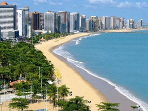Un paysage urbain côtier avec une plage de sable, des palmiers et de hauts immeubles.