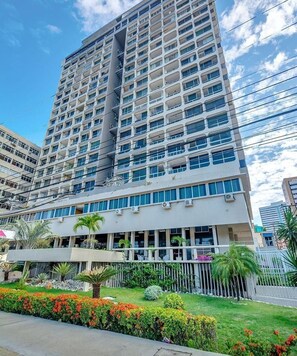 Un hôtel à plusieurs étages doté d’une architecture moderne, avec des balcons, de grandes fenêtres et un jardin bien entretenu.