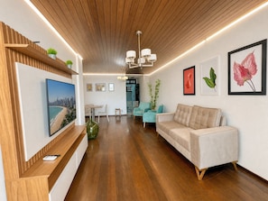 A modern living room with a wooden ceiling, a large flat-screen TV, a sofa, and a dining area with a table and chairs. - Top Beira Mar 4 Quartos Vista Espetacular (Fortaleza)