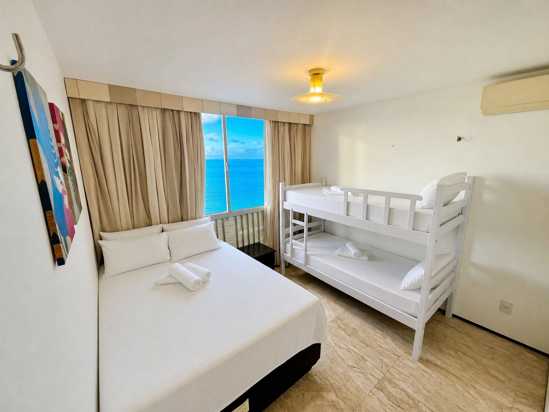 A hotel room with a bed, a bunk bed, a window with a view of the sea, and a ceiling light.