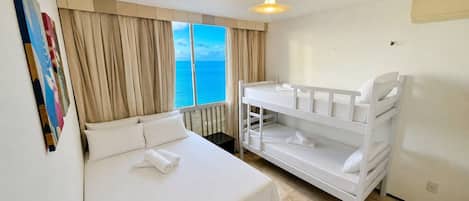 A hotel room with a bed, a bunk bed, a window with a view of the sea, and a ceiling light.