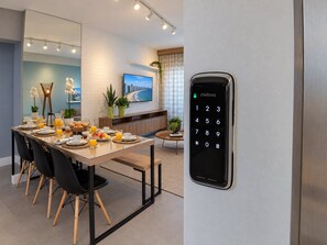 Una habitación de hotel moderna con zona de comedor, televisor y cerradura electrónica en la pared.