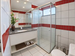 Une salle de bain moderne avec une douche à parois de verre, un lavabo blanc et des murs recouverts de carreaux rouges.