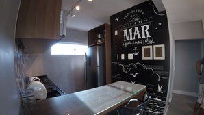 Une cuisine moderne avec une table à manger au plateau en verre, des appareils électroménagers en acier inoxydable et une fresque murale décorative.
