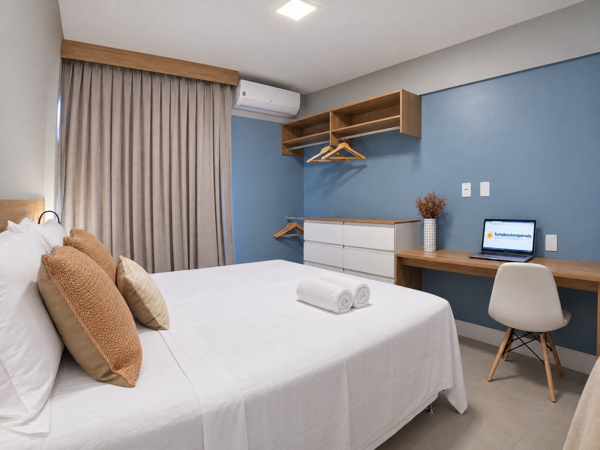 Une chambre d’hôtel avec un lit, un bureau, une chaise, un ordinateur portable et une fenêtre avec des rideaux.