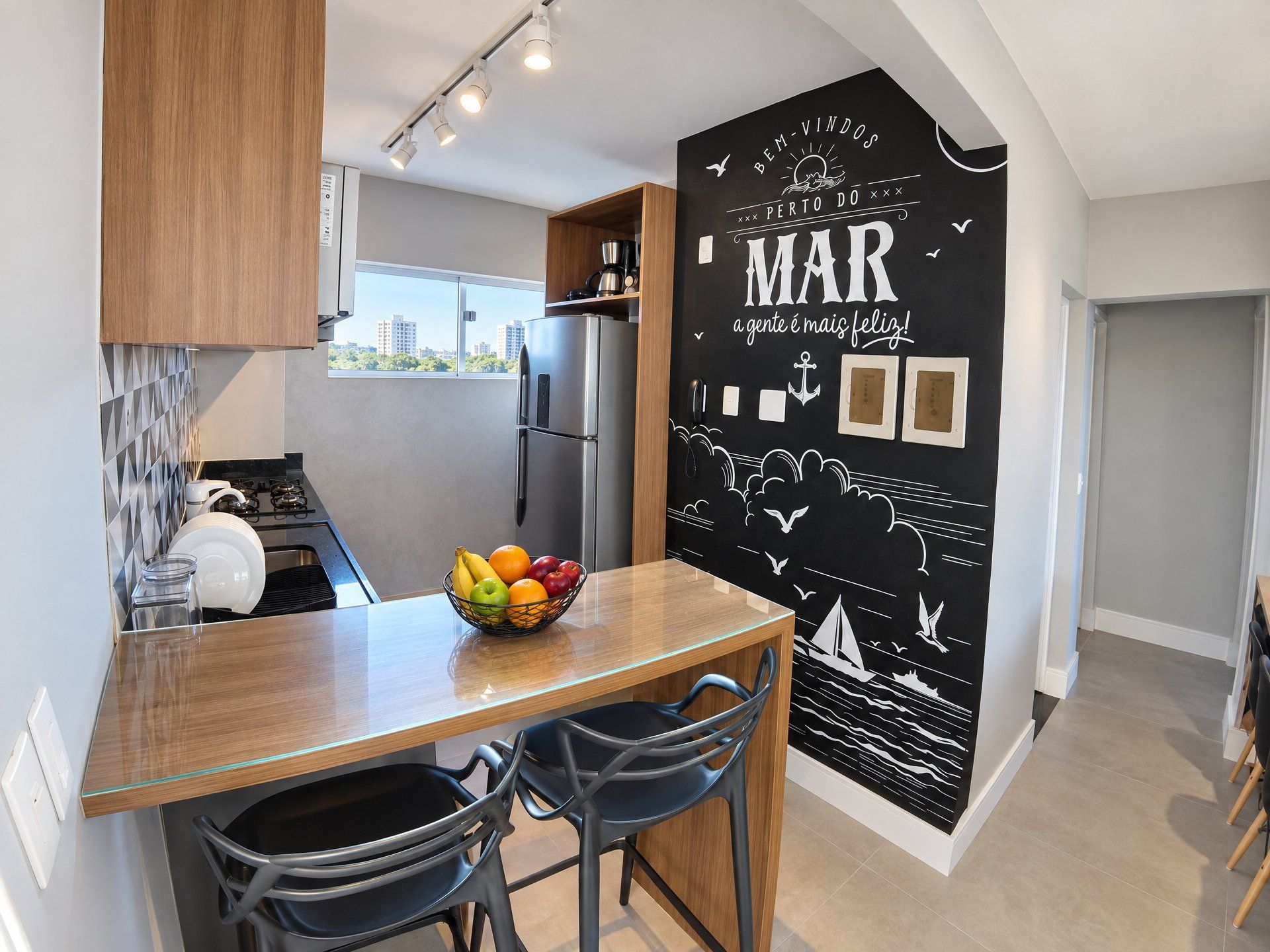 A modern kitchen with a wooden countertop, a fruit bowl, and a black wall with maritime-themed artwork.
