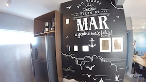 Une cuisine avec un réfrigérateur noir, des étagères en bois et un mur décoré d’œuvres d’art sur le thème de la mer.