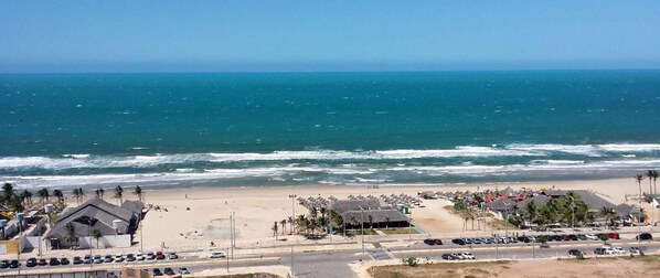 A beachside view with a parking lot, beach umbrellas, and a clear view of the ocean. - Beautiful Apartment With sea View 2 Bedrooms (Fortaleza)