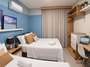 Une chambre d’hôtel comprenant un lit, un bureau avec un ordinateur portable, une table de chevet avec une lampe, un climatiseur fixé au mur et une fenêtre donnant sur la mer.