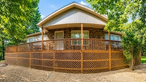 A two-story house with a stone facade, a wooden deck, and a fenced area. - Ozark Calling -- Ride-In Ride-Out MTB Basecamp, Premium Location (Bella Vista)