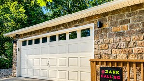 A garage with a white door, a stone wall, and a sign that reads 'ZARK CALLING.' - Ozark Calling -- Ride-In Ride-Out MTB Basecamp, Premium Location (Bella Vista)