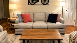 A living room with a sofa, a coffee table, a lamp, and a wall-mounted bicycle artwork. - Ozark Calling -- Ride-In Ride-Out MTB Basecamp, Premium Location (Bella Vista)