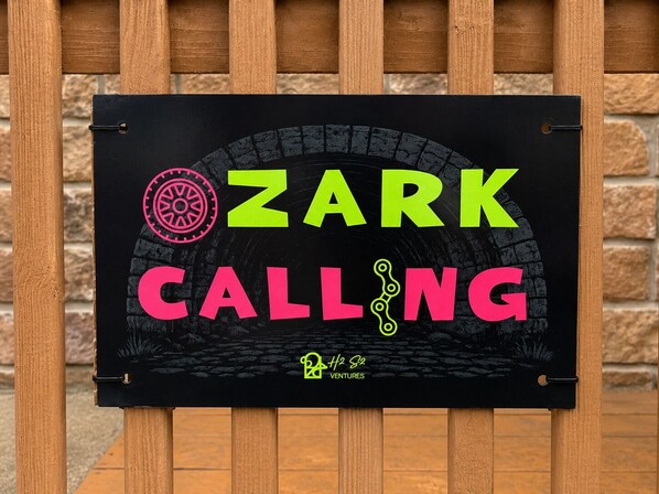 A black sign with 'ZARK CALLING' in bright colors, a logo, and 'H2O Ventures' text. - Ozark Calling -- Ride-In Ride-Out MTB Basecamp, Premium Location (Bella Vista)