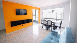 A modern living room with a large TV, a dining area, and a balcony with a view. - Departamento moderno Edimar 202 (Magdalena)