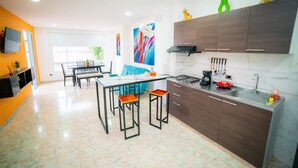 A modern kitchen with a gas stove, a coffee maker, and a sink. There is a dining area with a blue sofa and a table. - Departamento moderno Edimar 202 (Magdalena)