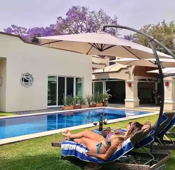 A poolside area with a pool, lounge chairs, and an umbrella.