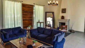 Un salón con dos sofás oscuros, una mesa de centro de madera, una araña, una chimenea y un espejo grande.