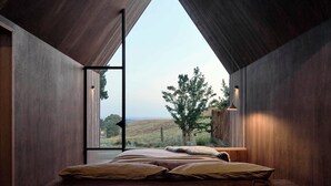 Un dormitorio con un ventanal grande, una cama y vistas a un árbol y colinas.