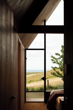 A room with a large window, a bed, and a view of a grassy landscape.