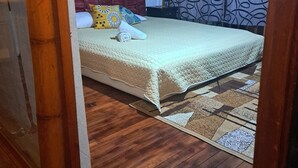 A room with a bed, a wooden floor, a patterned wall, and a door.