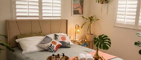 Ein Schlafzimmer mit einem Bett, einem Deckenventilator, einem Nachttisch mit Lampe und zwei Fenstern mit Jalousien.