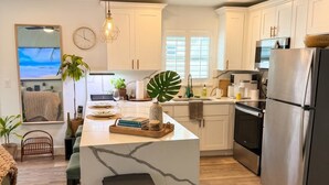 Una cocina moderna con armarios blancos, una isla de mármol, electrodomésticos de acero inoxidable y un ventanal grande.