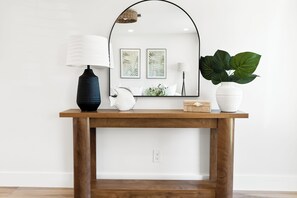 A wooden console table with a lamp, a white vase with a plant, and framed artwork on the wall.