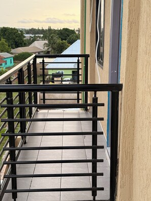 A balcony with a metal railing, a tiled floor, and a view of buildings and trees in the background. - Modern 2BR Apartment | Starlink Wi-Fi | Free Parking (Tamale)