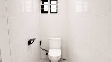 A narrow bathroom with white tiles, a toilet, a small window, and a trash bin.