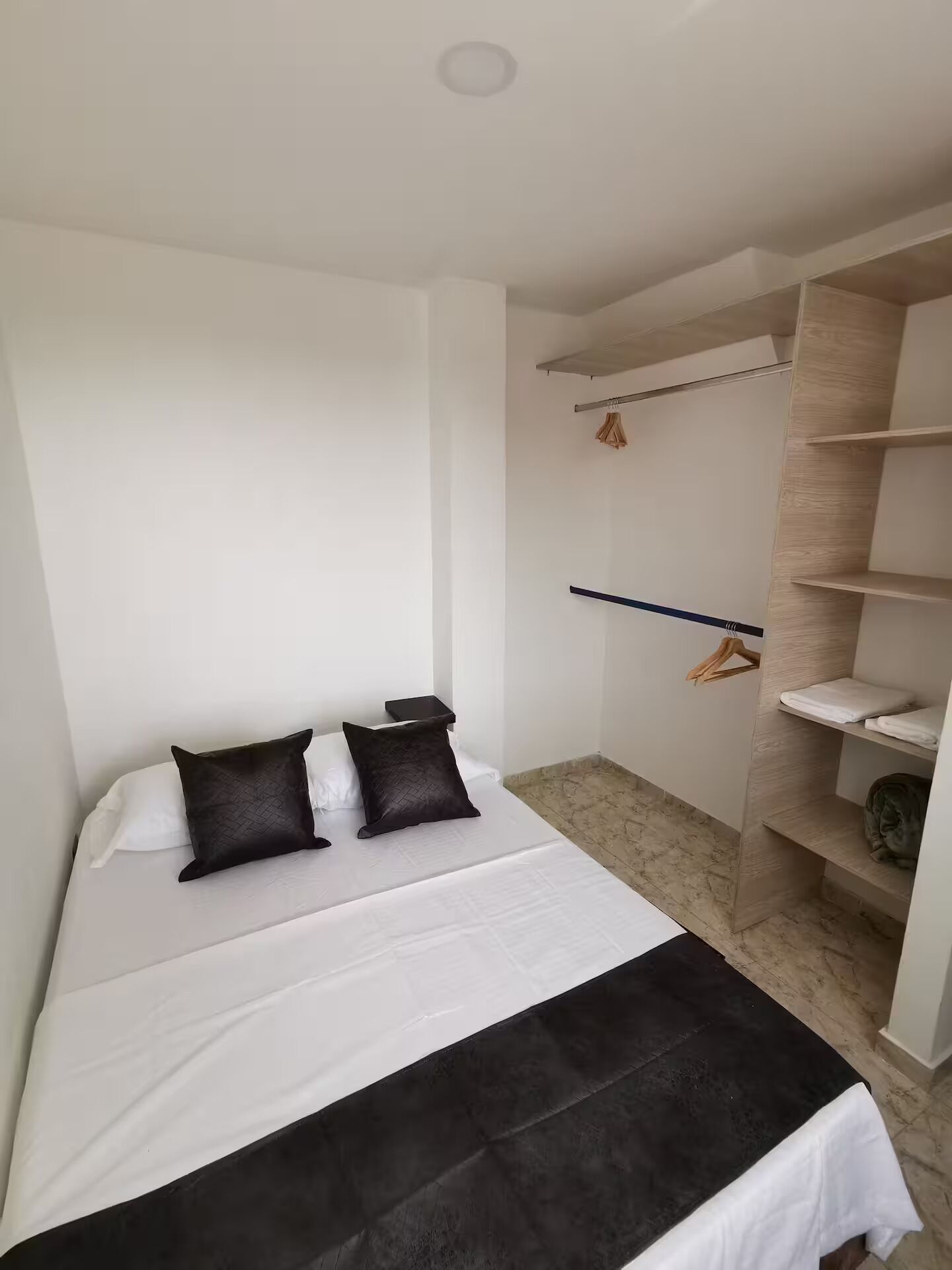Een slaapkamer met een bed, twee kussens, een nachtkastje, een kledingkast en een hangroede.