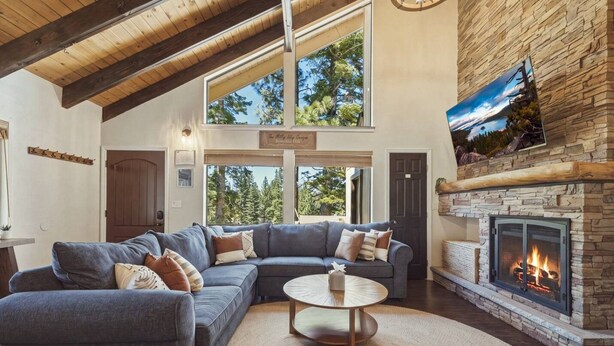 A living room with a stone fireplace, a large sectional sofa, and a television mounted on the wall. - Cozy Alpine Retreat | BBQ, Views + Fireplace (Stateline)