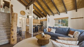 A spacious living area with a wooden ceiling, a sofa set, a coffee table, and a staircase.
