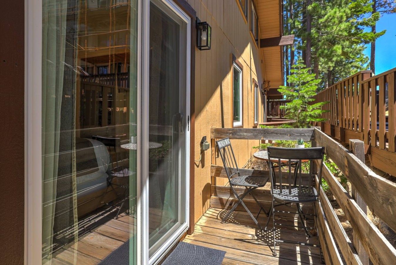 Eine Holzterrasse mit einer Glastür, die zu einem Raum führt, einem Tisch mit Stühlen und einem Holzzaun.